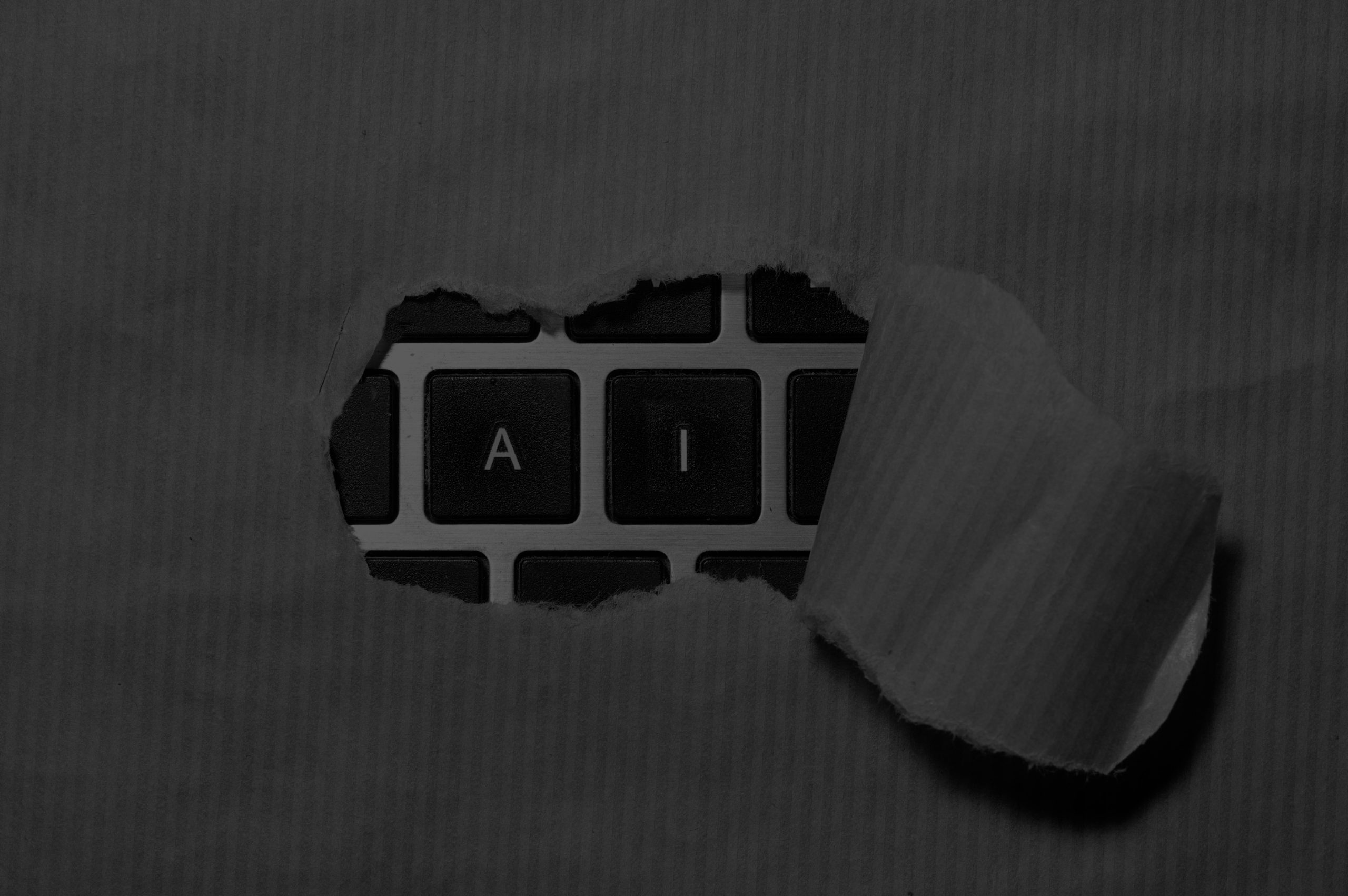 Black-and-white image of AI keyboard keys revealed through torn paper, representing PR and content optimization for AI search visibility in consumer tech.